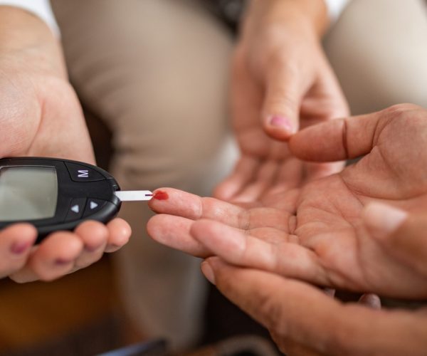 Female doctor checking senior woman's blood sugar at home close-up, unrecognizable people